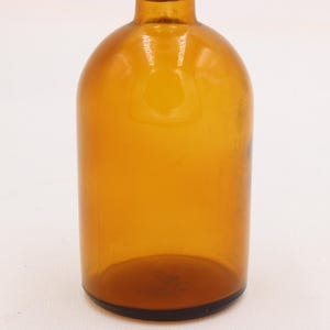 May include: Amber glass bottle with a rounded body and a narrow neck. The bottle has a dark brown base and a smooth, glossy surface. The bottle is empty and appears to be vintage.