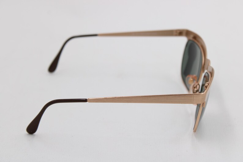 May include: Rose gold-toned sunglasses with dark lenses. The frames have a rectangular shape with a subtle, brushed finish. The temples are slender and end with dark brown tips. A classic accessory.