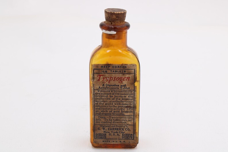 May include: An antique amber glass bottle with a cork stopper. The label reads "Trypsogen" and describes it as a digestive and anti-glycemic tablet. The bottle is marked with "Made in U.S.A."