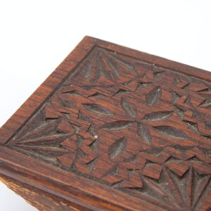 May include: Close-up of a dark brown wooden box with intricate floral carvings. The box has a rectangular shape with a detailed pattern of carved flowers and leaves. The wood has a rich, warm tone, and the carvings add depth and texture.