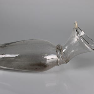 May include: A clear glass bottle with a unique shape, featuring a wide, flared opening and a slender neck. The bottle has a slightly curved body and a smooth, reflective surface. The design is elegant and modern.