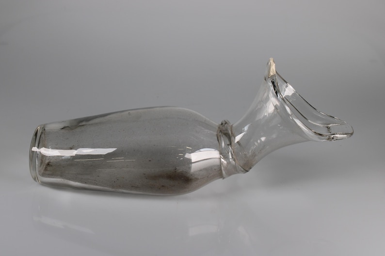 May include: A clear glass bottle with a unique shape, featuring a wide, flared opening and a slender neck. The bottle has a slightly curved body and a smooth, reflective surface. The design is elegant and modern.