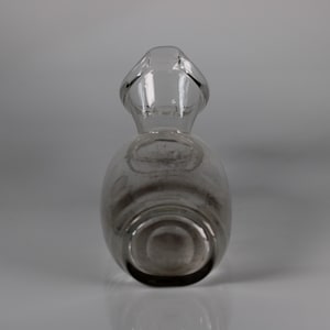May include: A clear glass decanter with a handle. The decanter has a rounded body and a narrow neck that leads to a handle. The glass is transparent, allowing a view of the contents. The decanter is likely used for serving beverages.
