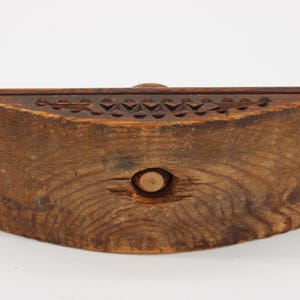 May include: A handcrafted wooden box with a curved front. The box is made of dark brown wood, featuring a carved geometric pattern along the top edge and a circular indentation in the center. The wood grain is visible.