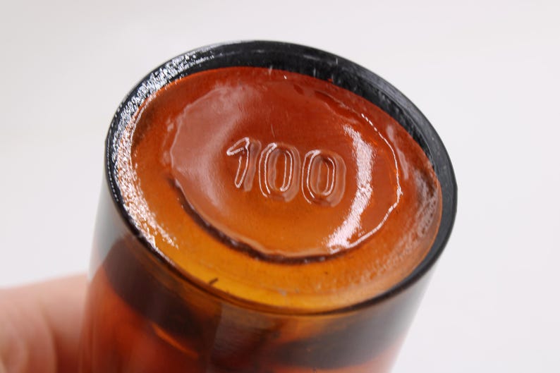 May include: Close-up of the bottom of a brown glass bottle. The number "100" is embossed on the base. The bottle has a dark rim and a glossy, amber-colored interior.