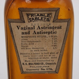 May include: An antique amber glass bottle with a paper label. The label reads "Friable Tablets Vaginal Astringent and Antiseptic." The label also lists ingredients and instructions. The bottle is likely from the early 20th century.