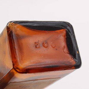 May include: Close-up of the bottom of a brown glass bottle. The number "206" is embossed on the bottom of the bottle. The bottle has a rectangular shape with rounded corners.