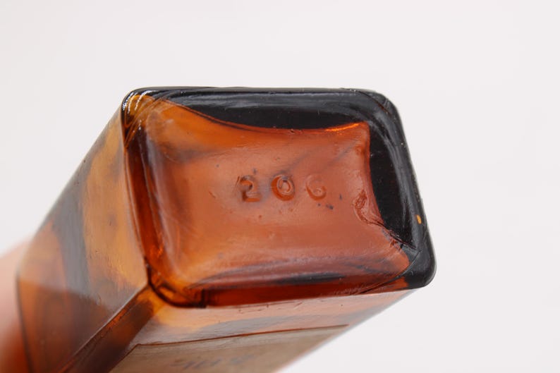 May include: Close-up of the bottom of a brown glass bottle. The number "206" is embossed on the bottom of the bottle. The bottle has a rectangular shape with rounded corners.
