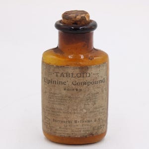 May include: An antique amber glass bottle with a cork stopper. The bottle has a paper label with the text "TABLOID Epinine Compound POISON". The bottle is a vintage apothecary item.