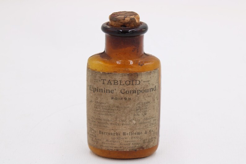 May include: An antique amber glass bottle with a cork stopper. The bottle has a paper label with the text "TABLOID Epinine Compound POISON". The bottle is a vintage apothecary item.