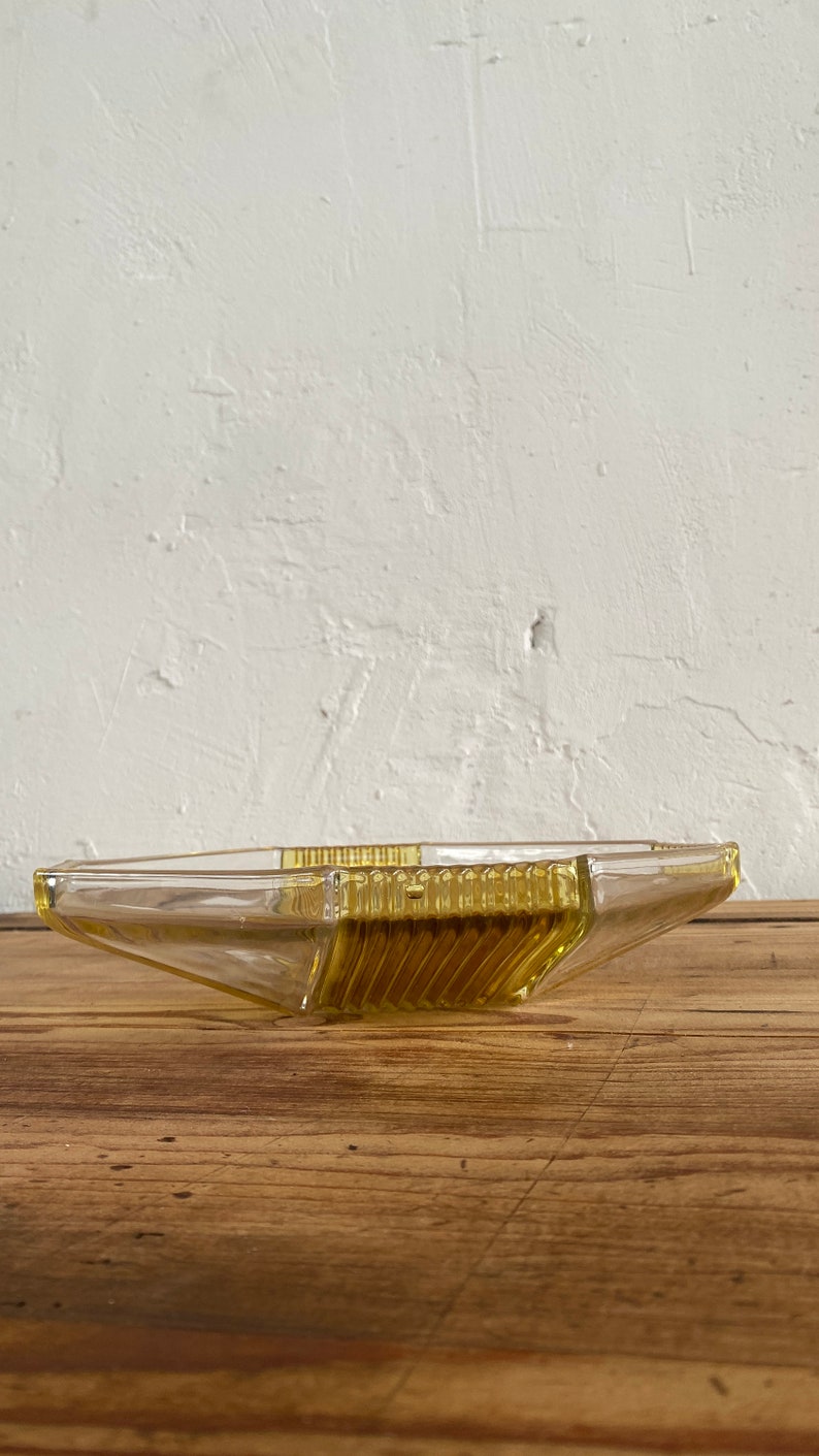 May include: A yellow glass serving dish with a geometric design. The dish is made of clear glass with a yellow tint and has a starburst pattern.