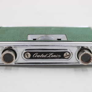 May include: A vintage pair of silver-toned opera glasses with a green textured top. The binoculars have a central focus wheel and the text "Coated Lens 2.5x" is visible on the front.