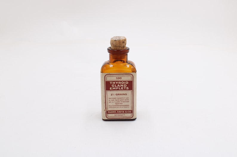 May include: An amber-colored glass bottle with a cork stopper. The bottle has a rectangular label with the text "100 Thyroid Gland Emplets 2 1/2 Grains" and the brand "PARKE, DAVIS & CO. SYDNEY".