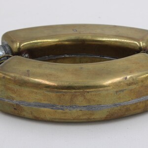 May include: A vintage brass flask with a curved, rectangular shape. The flask is made of brass with a tarnished, aged appearance. It has two screw-on caps and a silver-colored seam. The flask is likely used for carrying liquids.