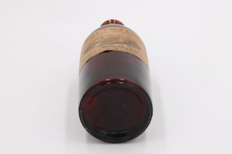 Puede incluir: Una botella de vidrio marr&oacute;n vintage con una etiqueta. La botella tiene una forma redondeada y un color &aacute;mbar oscuro. La etiqueta parece tener texto y es de color marr&oacute;n claro. La botella est&aacute; acostada de lado.