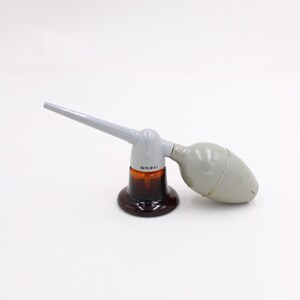 May include: A vintage atomizer with a brown glass base and a gray bulb and nozzle. The text "DEVILBISS" is printed on the base. The atomizer is designed to spray liquids.