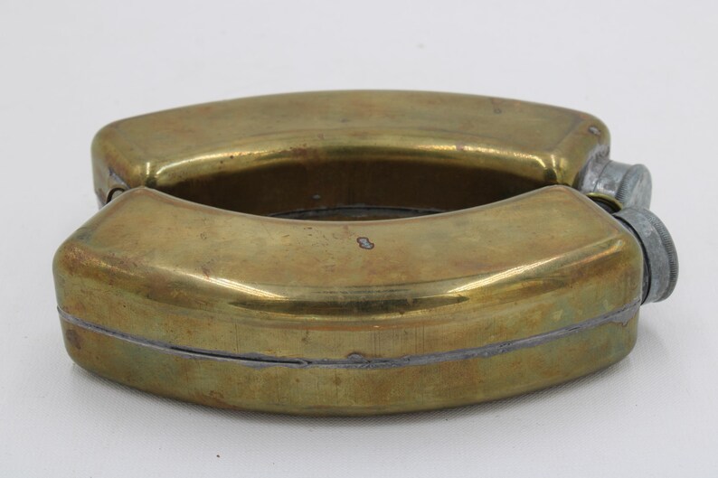 May include: A vintage brass flask with a hinged design. The flask has a rounded shape with a tarnished finish and two screw-on caps. The overall design is a classic, functional piece.