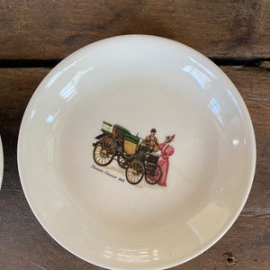 Puede incluir: Un platillo de cerámica blanca con una ilustración vintage de un automóvil Packard-Leasure 1893 con un hombre y una mujer con ropa de época. El platillo tiene un diámetro de 15 cm.