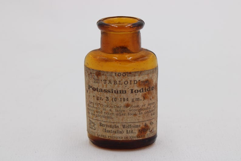 Puede incluir: Una botella de vidrio &aacute;mbar con una etiqueta que dice "TABLOID Potassium Iodide". La etiqueta tambi&eacute;n incluye instrucciones de dosificaci&oacute;n y el nombre del fabricante, Burroughs Wellcome & Co. Es un antiguo envase farmac&eacute;utico.