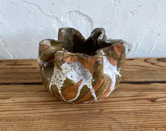 May include: A small, ceramic planter with a ruffled edge. The planter is decorated with a brown, green, and white glaze.