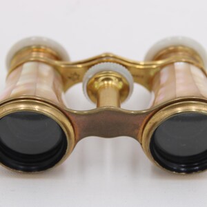 May include: Antique opera glasses with a gold-tone metal frame and mother-of-pearl accents. The lenses are black, and the binoculars have a central focus wheel. The design is ornate and vintage.
