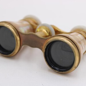 May include: Antique opera glasses with a brass frame and mother-of-pearl accents. The lenses are black, and the binoculars have a handle for easy grip. The design is vintage and elegant.