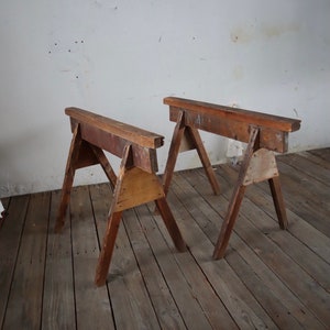 Könnte beinhalten: Zwei Holzbock, aus wiederverwendetem Holz gefertigt, stehen auf einem Holzboden. Die Böcke sind beide gleich groß und gleich geformt und beide in gutem Zustand.