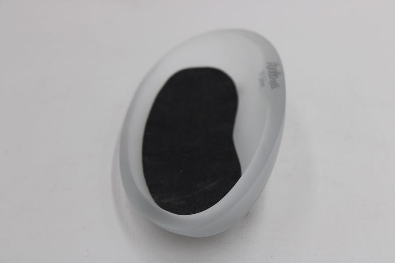 K&ouml;nnte beinhalten: Oval geformte Seifenschale aus mattiertem Glas mit schwarzem Einsatz. Die Schale hat ein glattes, geschwungenes Design und ein kleines Logo an der Seite. Die Seifenschale ist f&uuml;r Seifenst&uuml;cke konzipiert.
