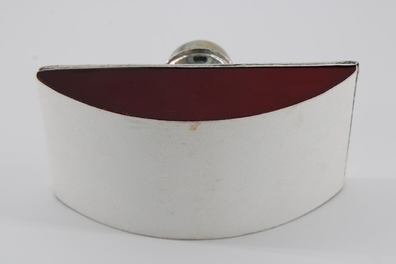 May include: A silver-colored flask with a curved, white body and a deep red top. A small, round, silver-colored stopper is visible at the top. The flask has a simple, elegant design.