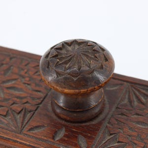 May include: Close-up of a dark brown wooden inkwell with a carved floral design. The inkwell features a round, carved knob on top. The wood has a rich, warm tone, and the carving is detailed.