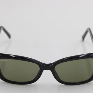 Puede incluir: Gafas de sol negras con montura de ojo de gato y lentes verdes. El logotipo de Ray-Ban es visible en la lente izquierda. Dise&ntilde;o elegante y moderno.