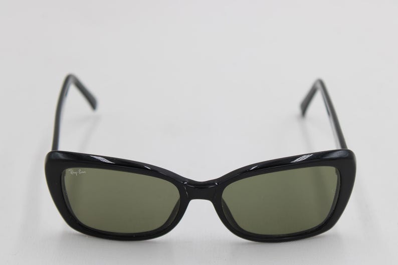 Puede incluir: Gafas de sol negras con montura de ojo de gato y lentes verdes. El logotipo de Ray-Ban es visible en la lente izquierda. Dise&ntilde;o elegante y moderno.