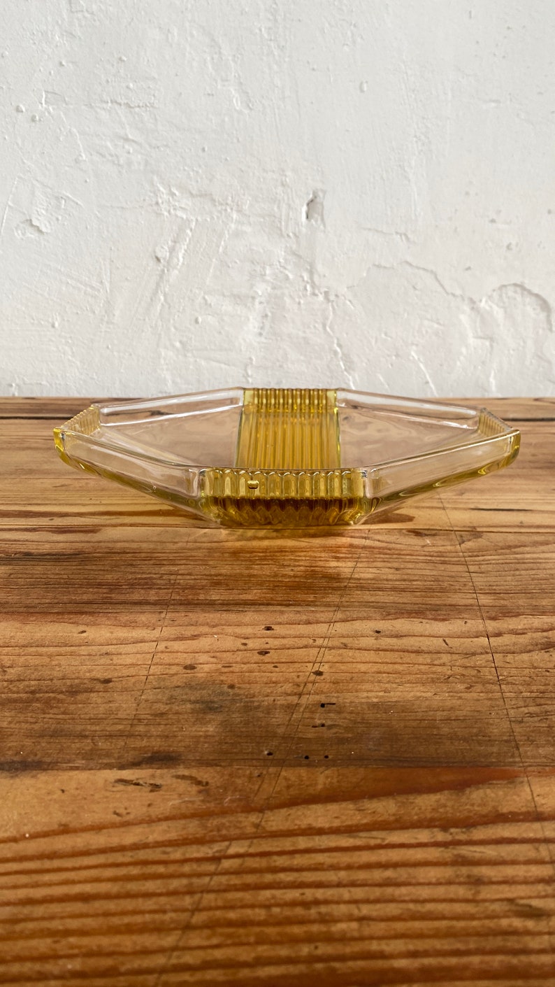 May include: A clear glass serving tray with a hexagonal shape and a raised, textured center section. The tray is a pale yellow color.