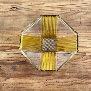 May include: A clear glass bowl with a geometric design. The bowl has a yellow-amber color and a textured surface. The bowl is sitting on a wooden surface.