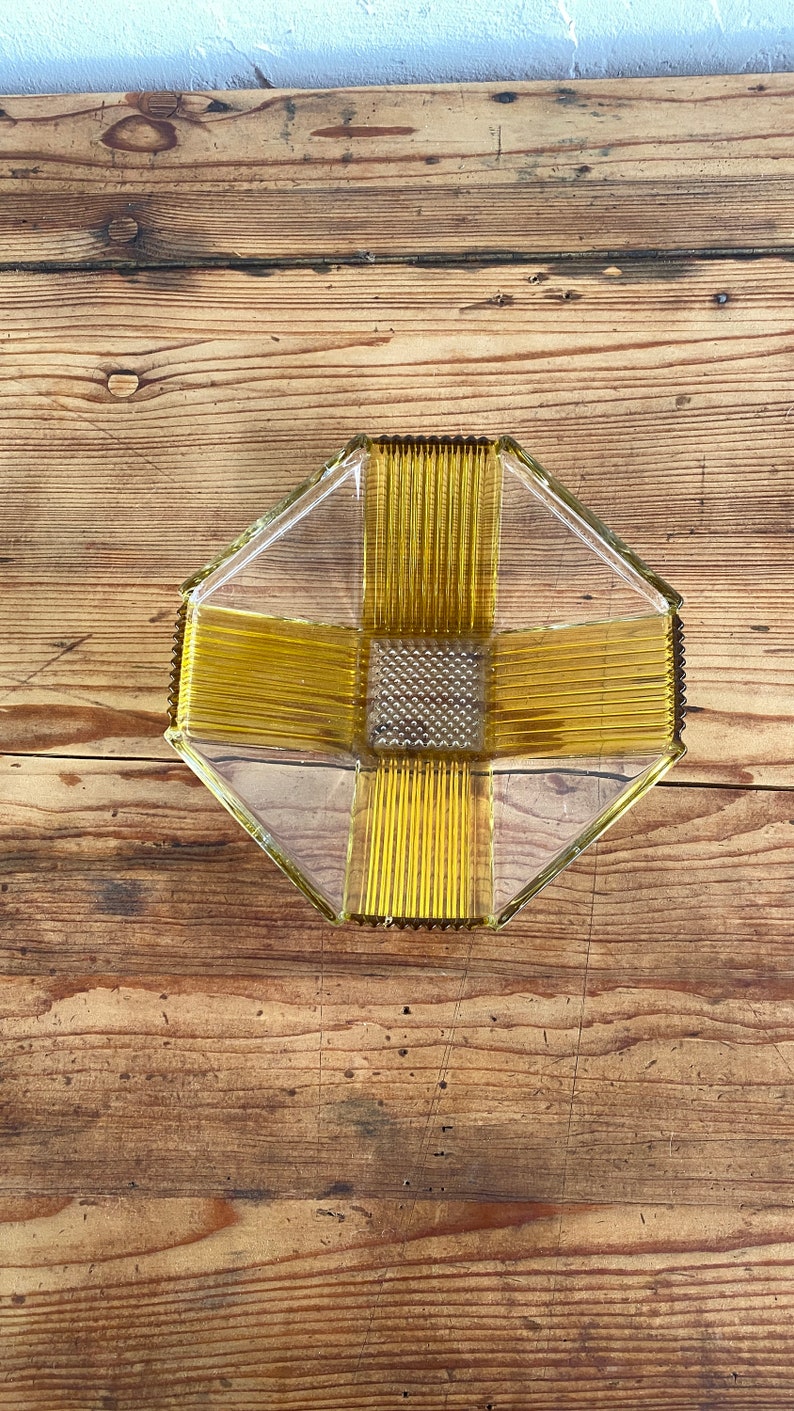 May include: A clear glass bowl with a geometric design. The bowl has a yellow-amber color and a textured surface. The bowl is sitting on a wooden surface.