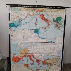 Op de afbeelding: Een vintage kaart getiteld "Rom und Karthago" en "Mische Reich zur Zeit Caesars" met gedetailleerde illustraties van oude gebieden. De kaart heeft een kleurgecodeerd ontwerp met tekst in het Duits en is gemonteerd op een zwarte staaf om op te hangen.