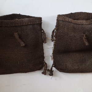 May include: Two brown woven bags with drawstrings hanging on a white wall.