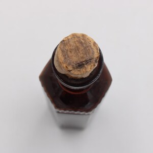 Puede incluir: Una botella de vidrio marr&oacute;n con un tap&oacute;n de corcho. La botella tiene forma hexagonal y es de color marr&oacute;n oscuro. El corcho es de color marr&oacute;n claro y texturizado.