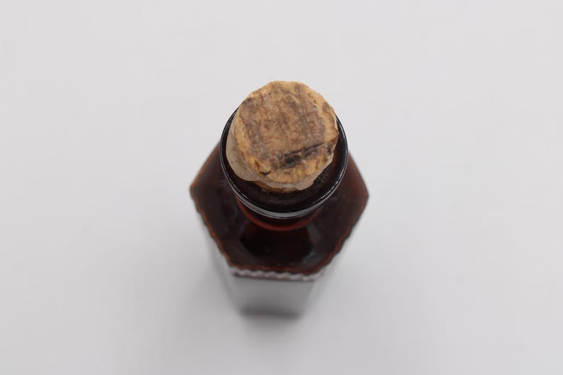 Puede incluir: Una botella de vidrio marr&oacute;n con un tap&oacute;n de corcho. La botella tiene forma hexagonal y es de color marr&oacute;n oscuro. El corcho es de color marr&oacute;n claro y texturizado.