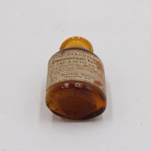 Puede incluir: Peque&ntilde;a botella de vidrio &aacute;mbar con tapa amarilla. La etiqueta, parcialmente visible, indica "Tabloids Potassium Iodide". La botella est&aacute; sobre una superficie blanca. Se aprecia el contenido.