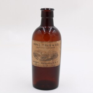 Puede incluir: Una botella de vidrio marr&oacute;n vintage con una etiqueta que dice "PARKE, DAVIS & CO. MANUFACTURING CHEMISTS DETROIT, MICHIGAN, U.S.A." La botella tiene un cuerpo redondeado y un cuello estrecho.