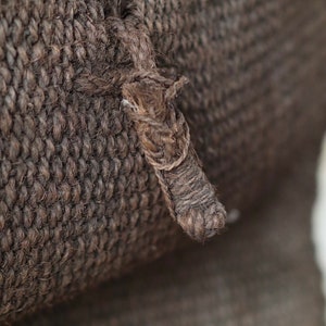 May include: Close-up of a brown woven fabric with a thick, knotted rope detail.