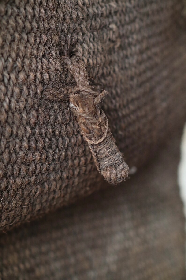 May include: Close-up of a brown woven fabric with a thick, knotted rope detail.