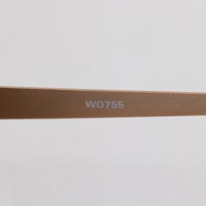 May include: Close-up of a pair of gold-colored sunglasses. The arm of the glasses is visible, with the text "W0755" printed on it. The hinge and the frame are also visible.