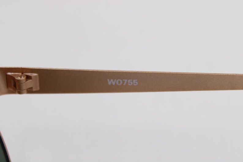 May include: Close-up of a pair of gold-colored sunglasses. The arm of the glasses is visible, with the text "W0755" printed on it. The hinge and the frame are also visible.