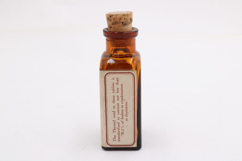 May include: A small, amber-colored glass bottle with a cork stopper. A rectangular label is affixed to the bottle, with text that reads: "The Thyroid used in these tablets is standardized to contain not less than '0.1% of Iodine in combination as thyroxine.'"