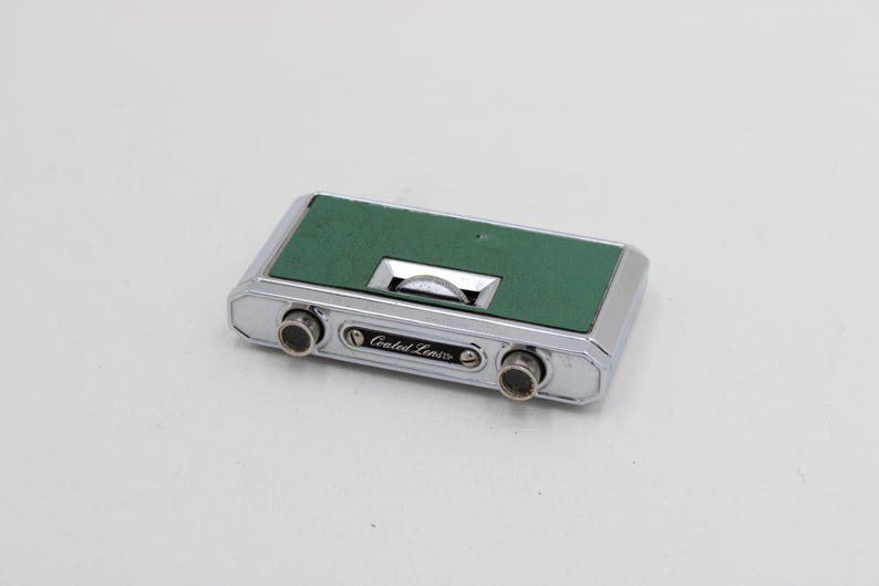 May include: A vintage pair of binoculars with a silver metal frame and a green leatherette top. The binoculars have two lenses and the text "Coated Lenses" is printed on the front.