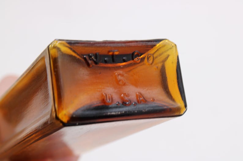 May include: Close-up of the bottom of a rectangular amber glass bottle. The base has embossed text that reads "W.T. & CO." above the number "6" and "U.S.A." below. The bottle has a vintage appearance.