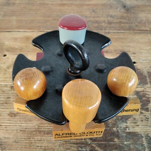 Peut inclure: Un tampon en m&eacute;tal noir vintage avec une poign&eacute;e, quatre boutons en bois et un dessus rouge et blanc. Le tampon est mont&eacute; sur une base en bois avec le texte "ALFRED CLOUTH Lackfabrik GmbH & Co. KG".