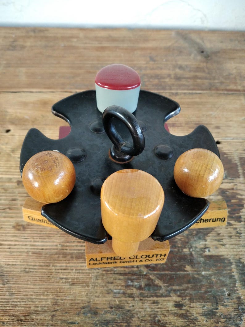 Peut inclure: Un tampon en m&eacute;tal noir vintage avec une poign&eacute;e, quatre boutons en bois et un dessus rouge et blanc. Le tampon est mont&eacute; sur une base en bois avec le texte "ALFRED CLOUTH Lackfabrik GmbH & Co. KG".